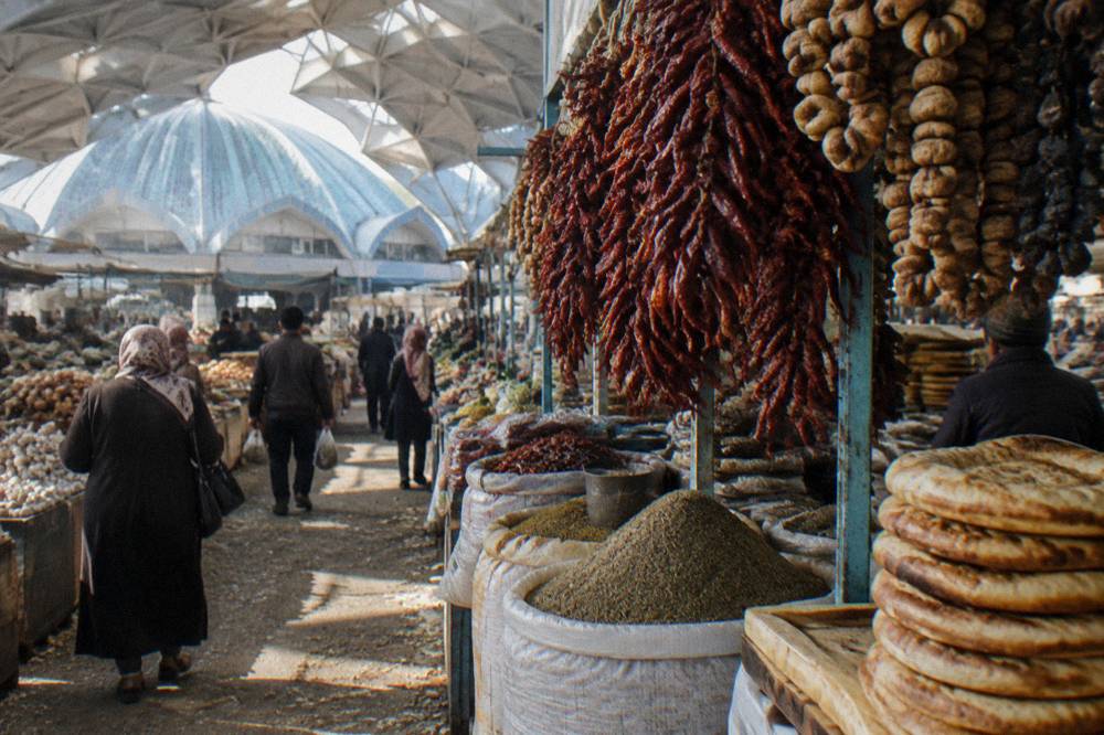 A crowded market aisle hung with spices, dried fruit and stacks of flatbread