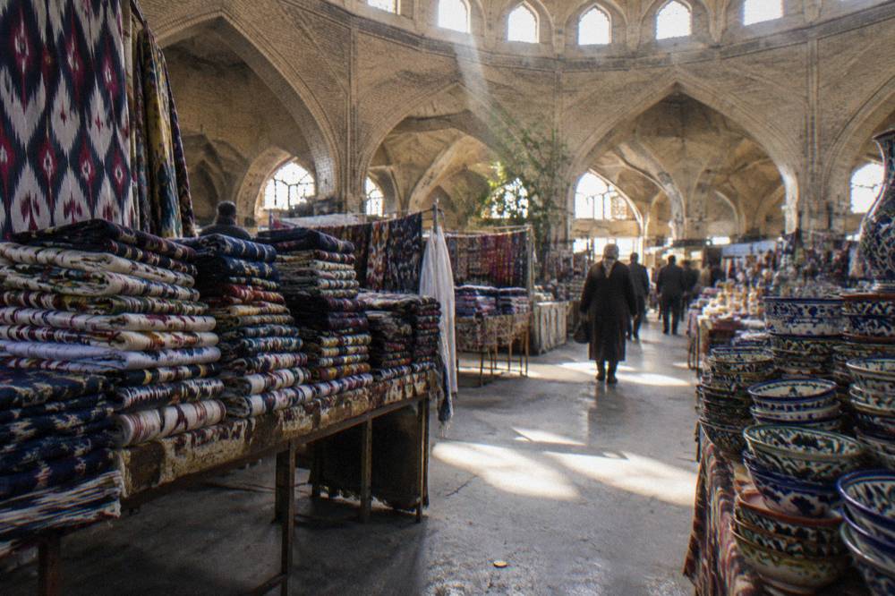 A covered bazaar interior with hanging textiles and stacked ceramics under brick vaults