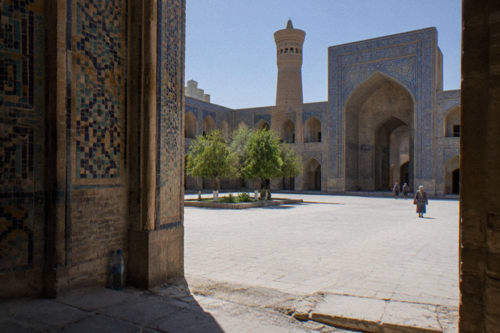 Sunlit courtyard of a madrasah in Bukhara with tiled arches and stone paving