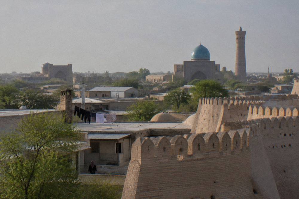 Blue-tiled dome and minaret rising above Bukhara's low-rise old city rooftops