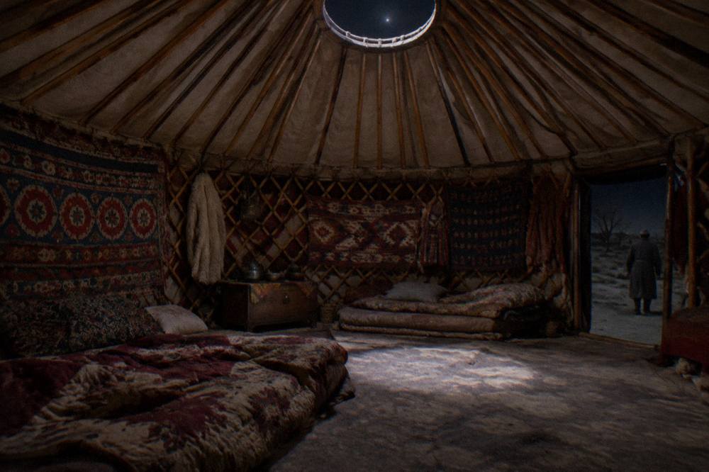 Interior of a round yurt with patterned textiles, low beds and a central skylight