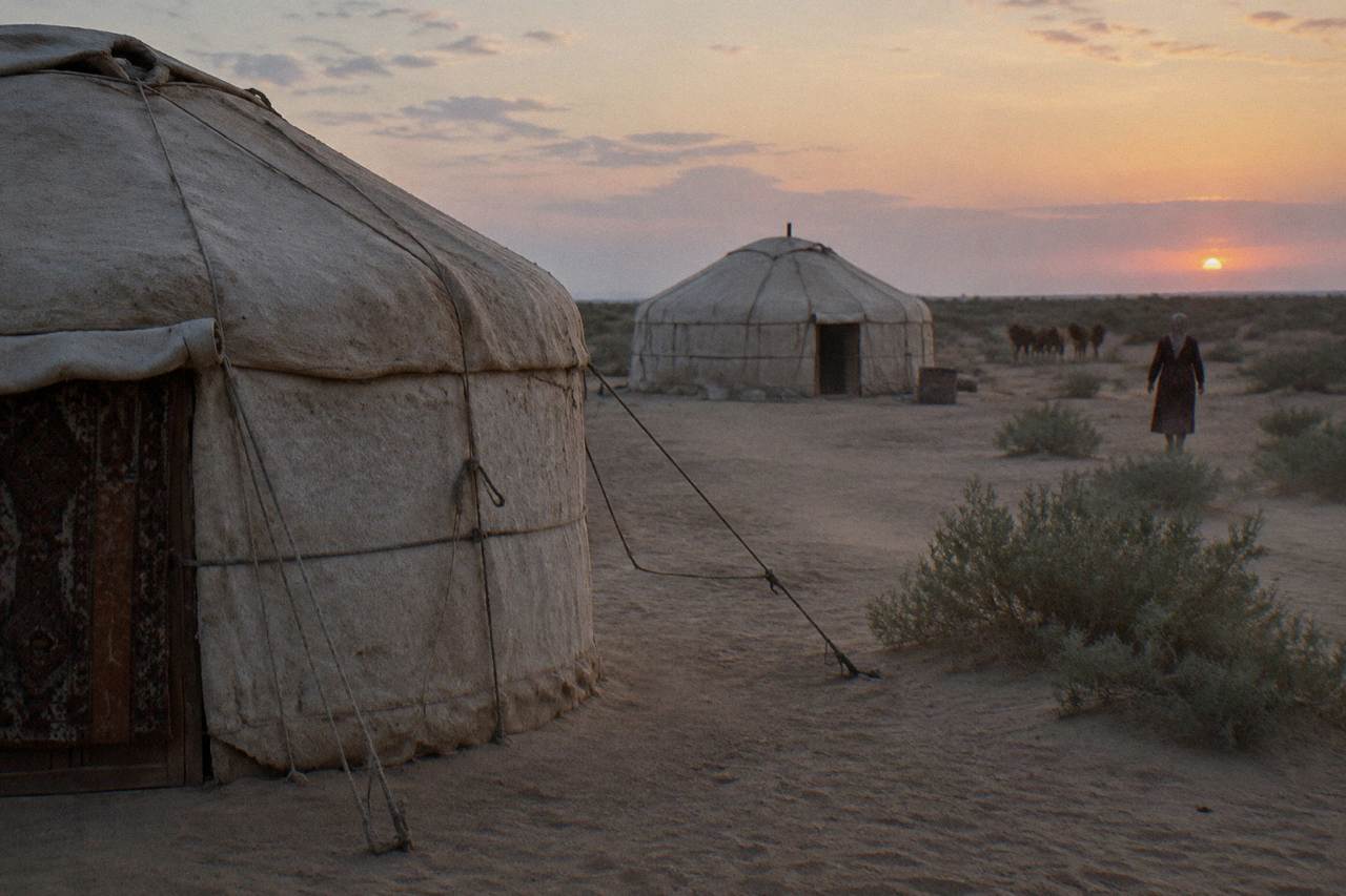 Round felt yurts standing on sand under a wide desert sky at dusk