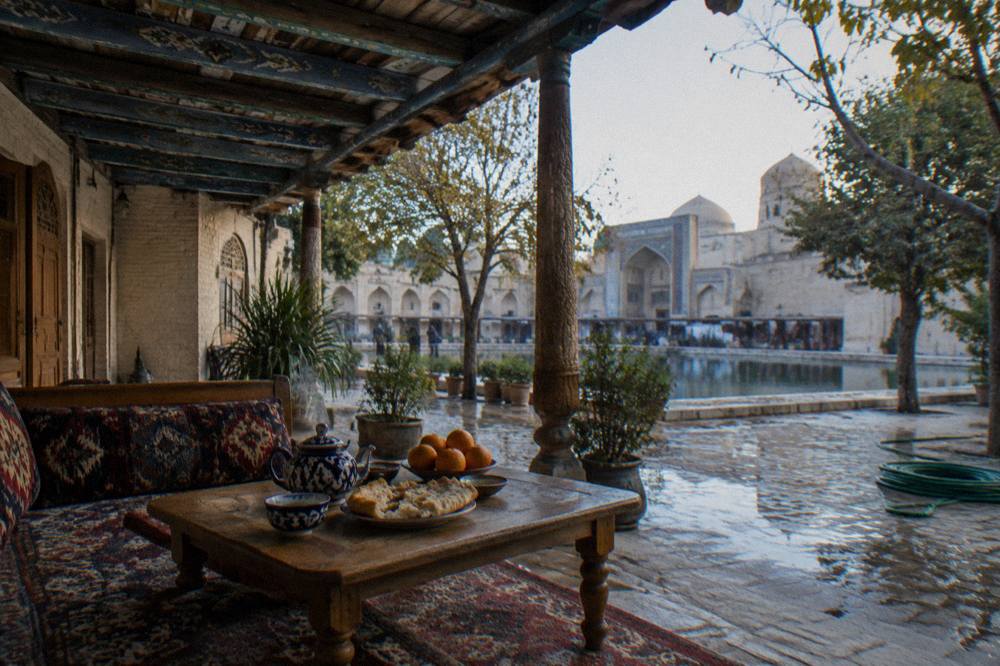 A guesthouse courtyard in Bukhara with a low table set with tea, bread and fruit