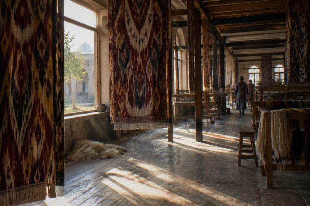 A workshop interior with handwoven silk carpets hanging from wooden beams