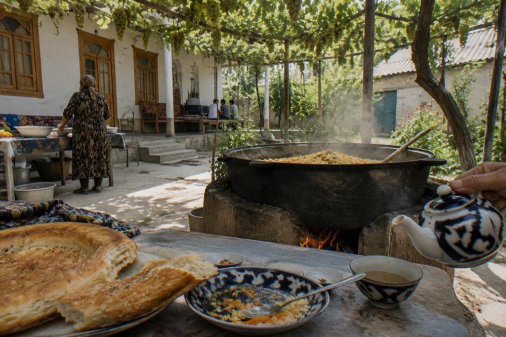A traditional Uzbek rice plov dish served on a table with flatbread and tea