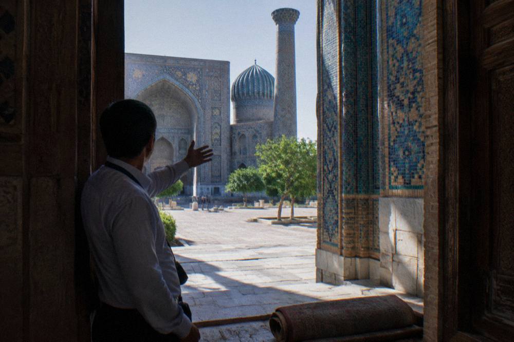 A guide leading a small group through a tiled courtyard of an old Silk Road monument
