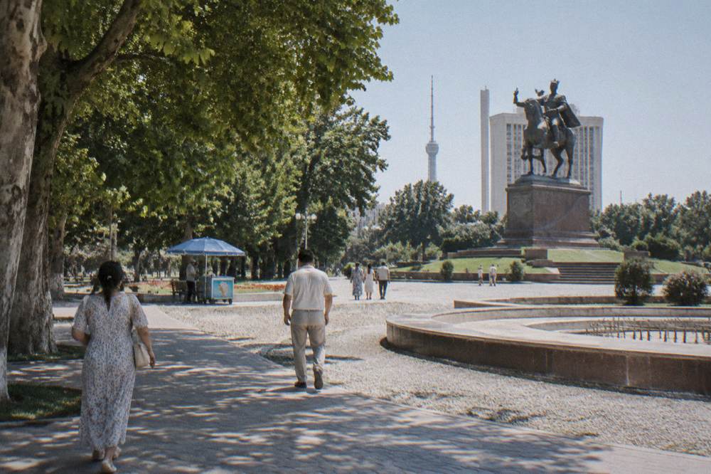 Travelers in light summer clothing walking along a broad plaza beside ancient tiled facades