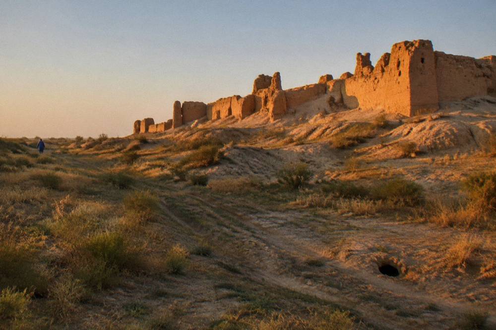 Ruined mud brick fortress walls standing alone in open desert grassland at golden hour