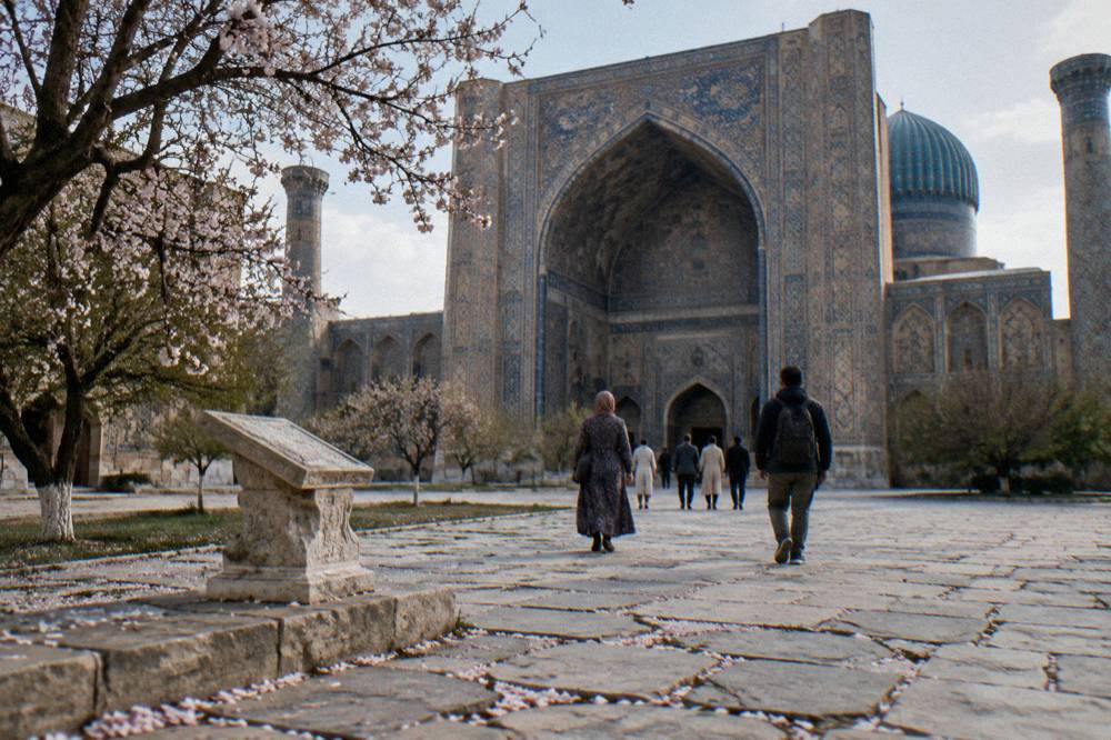 Travelers walking through a tiled courtyard of a Silk Road monument in Samarkand