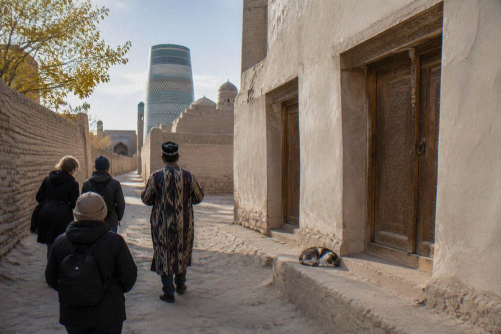 Guide leading a small group along a mudbrick wall inside Khiva's old city