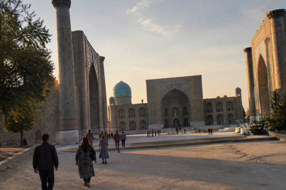Visitors walking across a wide plaza toward a tiled mosque facade in warm afternoon light