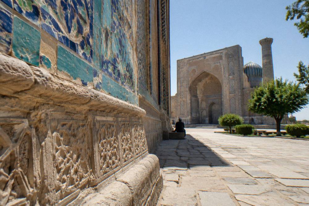 A wide stone plaza before a large tiled portal with blue domes under a clear sky