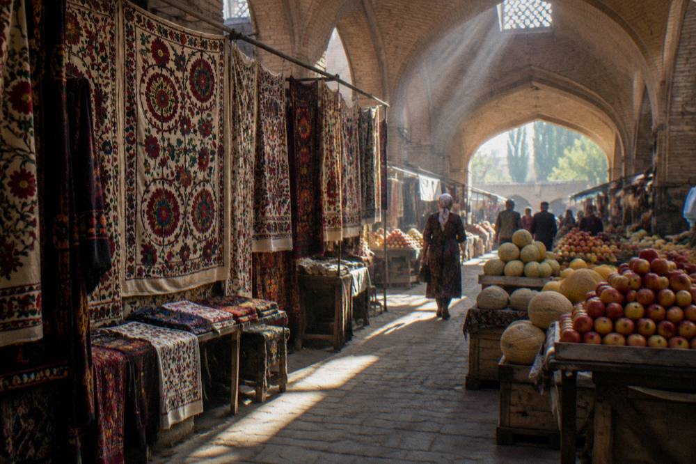 A covered market hall with hanging textiles and stacked fruit stalls