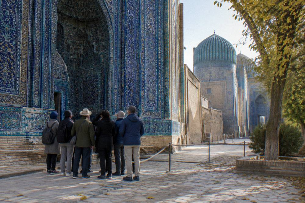 A small group with a guide standing before an ornate tiled entrance in an old city