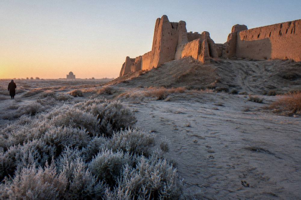 Ruined mud brick fortress walls rising from flat desert steppe under a wide sky