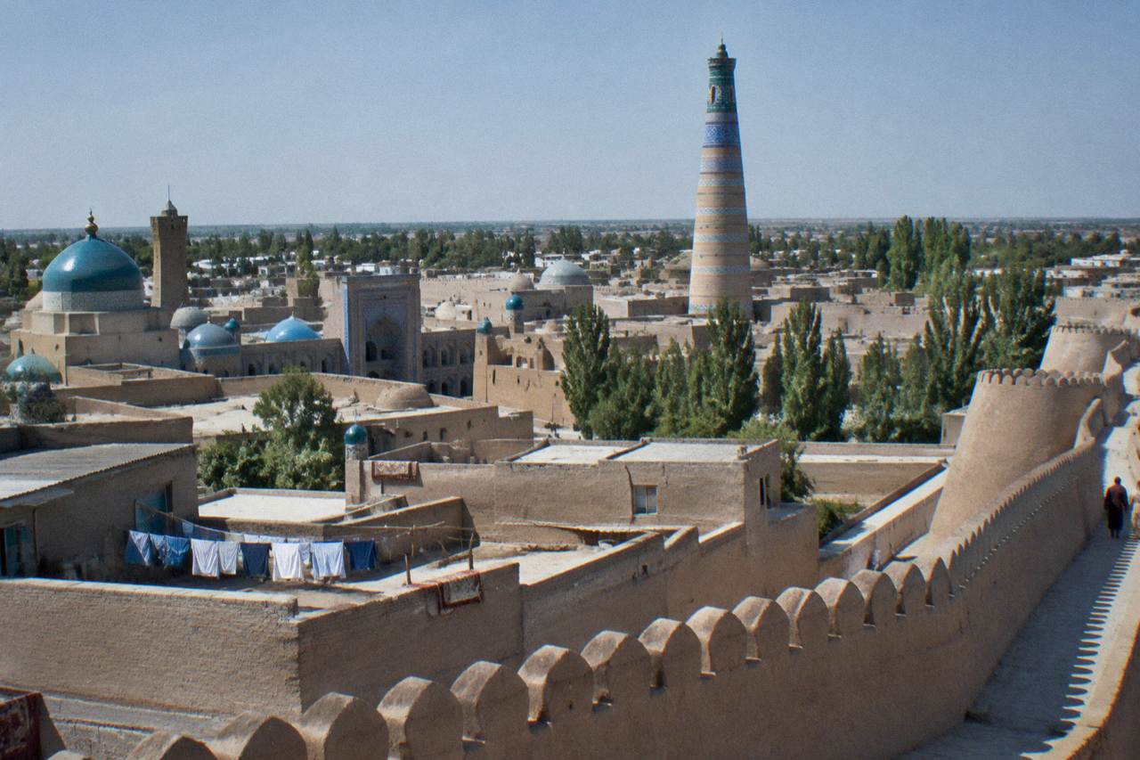 Mud brick walls and tiled minarets of an ancient walled city under a clear sky