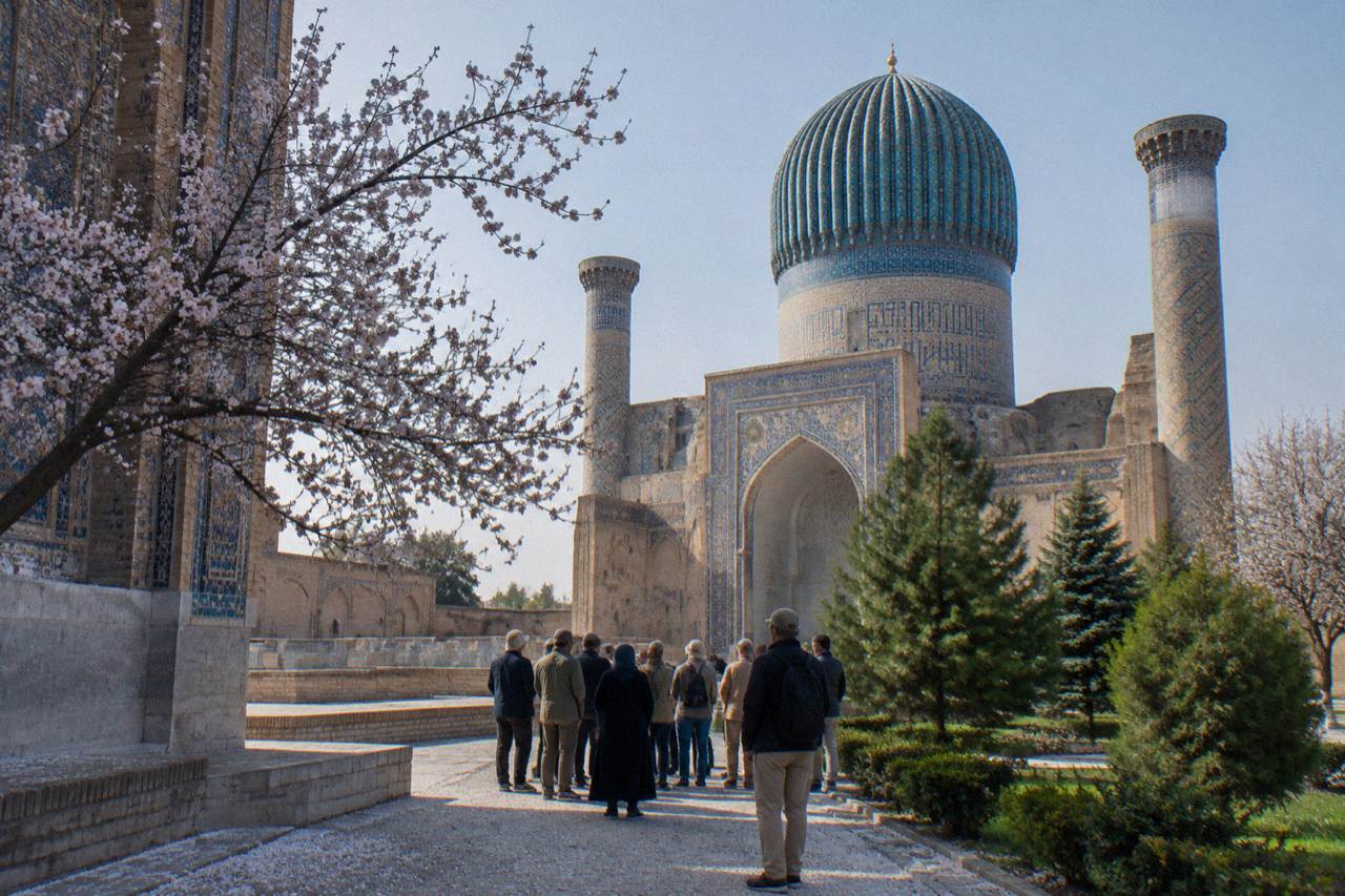 A guided tour group gathered in a tiled courtyard of an ancient Silk Road city under a blue domed monument