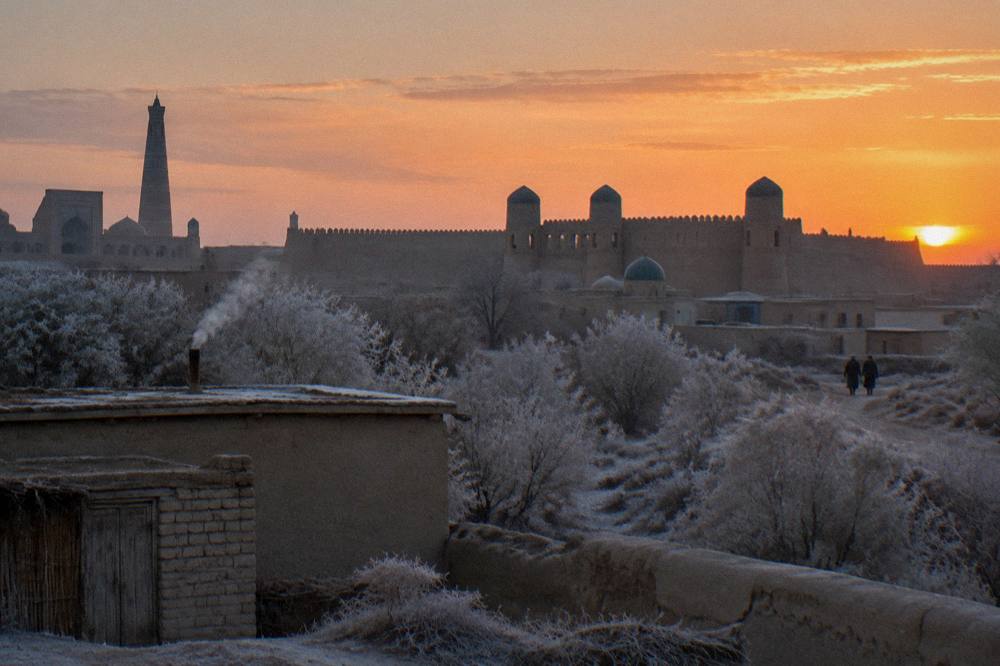 Ancient walled city silhouette at sunset with watchtowers against an orange sky