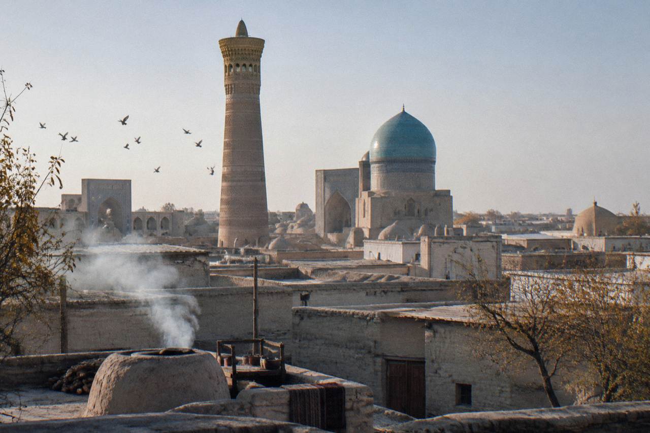 Blue tiled dome and minaret above an old city wall in Uzbekistan under a clear sky