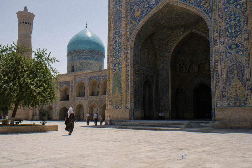 Ornate tiled portal of a medieval madrasah with turquoise dome behind it