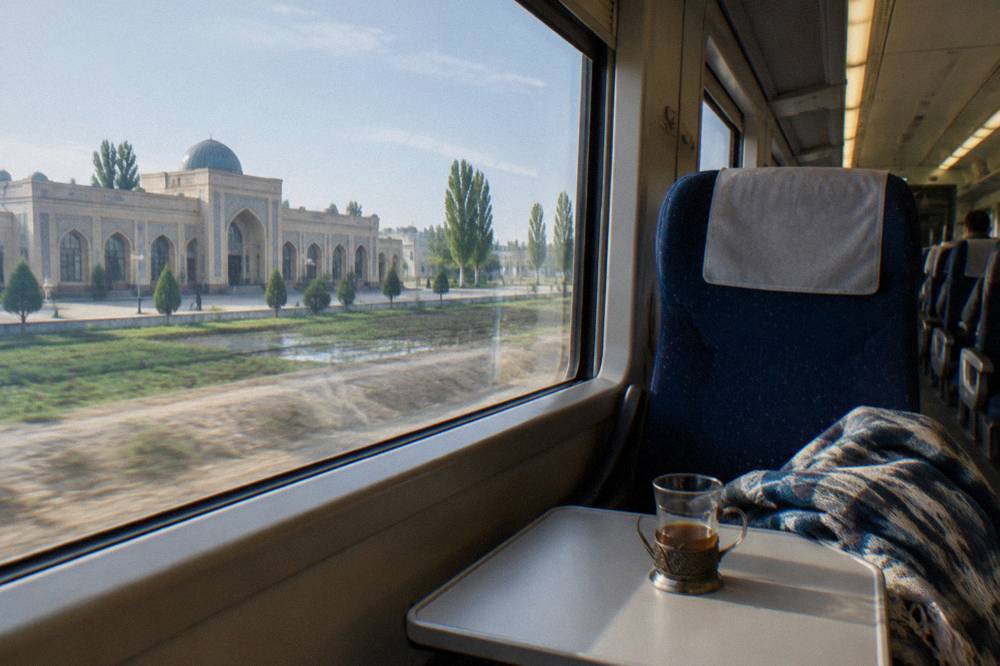 A bright modern train interior with reclining seats in rows and large windows showing open countryside