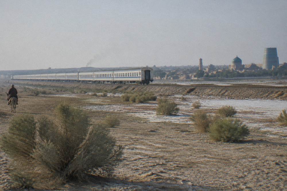 A long modern train traveling across flat desert steppe toward distant low mountains
