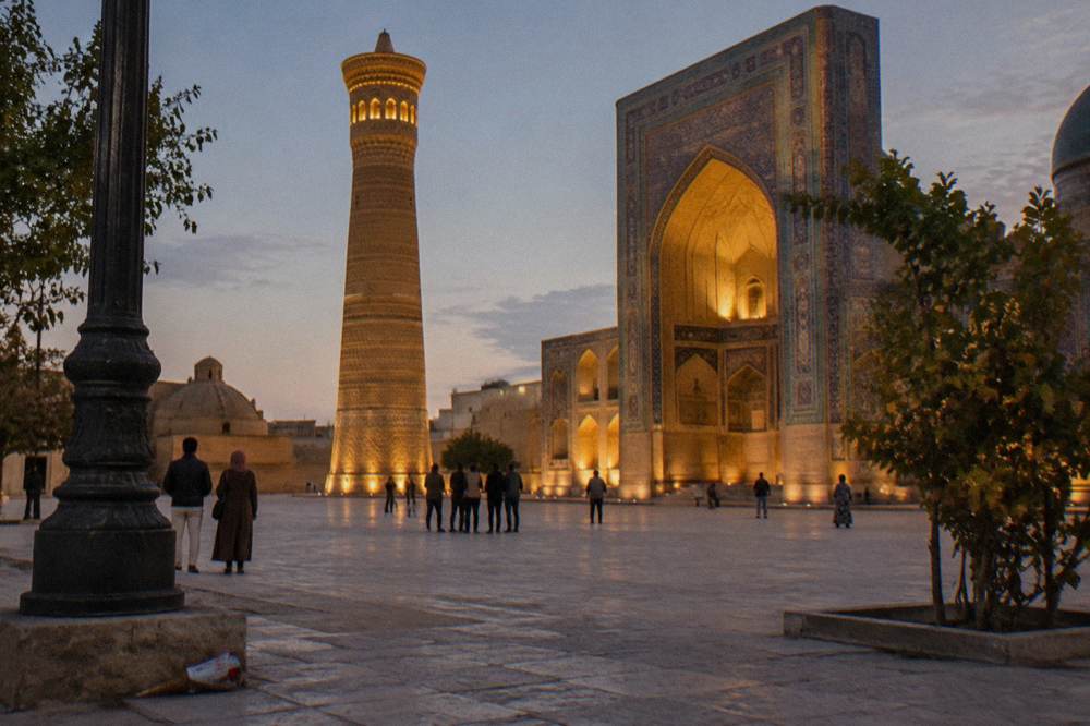 Evening crowd of travelers on a plaza beside a lit tiled monument in Bukhara
